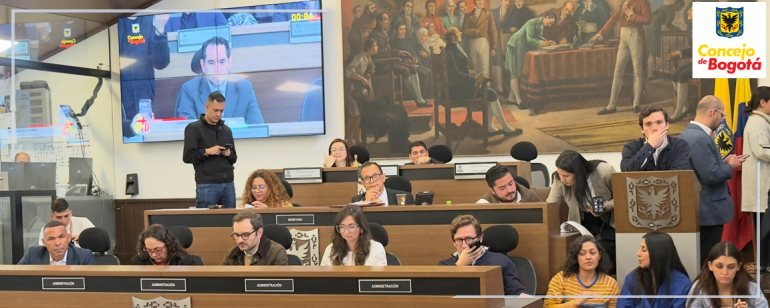 Personas sentadas en una mesa larga durante una sesión del Concejo de Bogotá con una pantalla de televisión al fondo