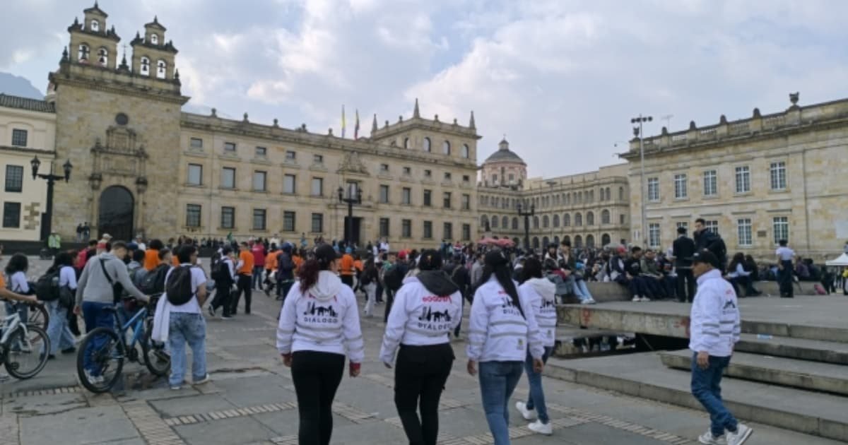 Personas caminando y sentadas en una plaza pública frente a edificios históricos de arquitectura clásica.